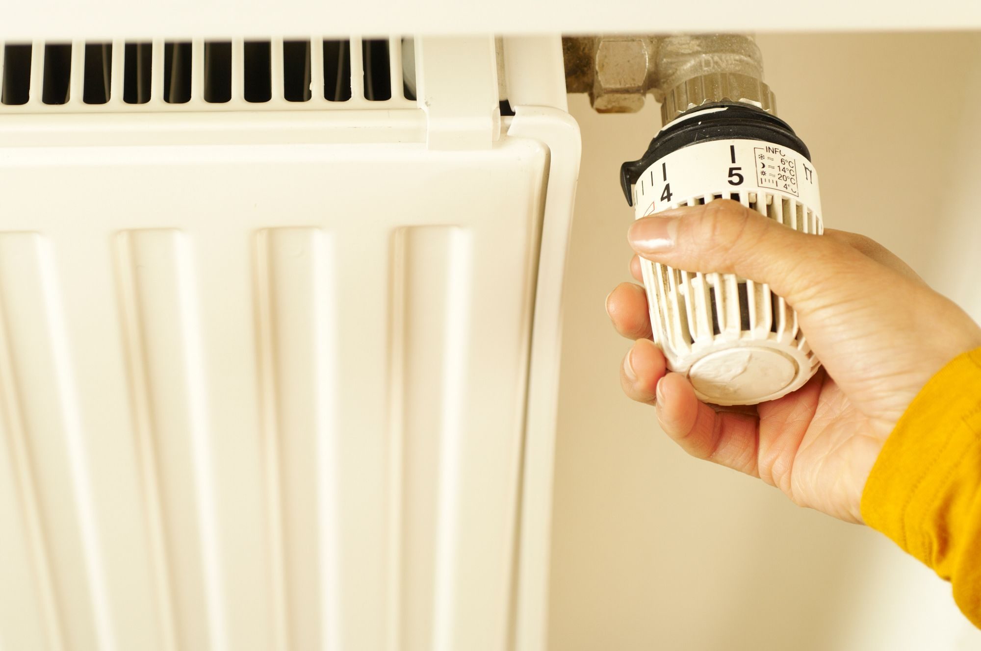 Hand in a yellow knitted sleeve turning the thermostatic valve on a cream radiator
