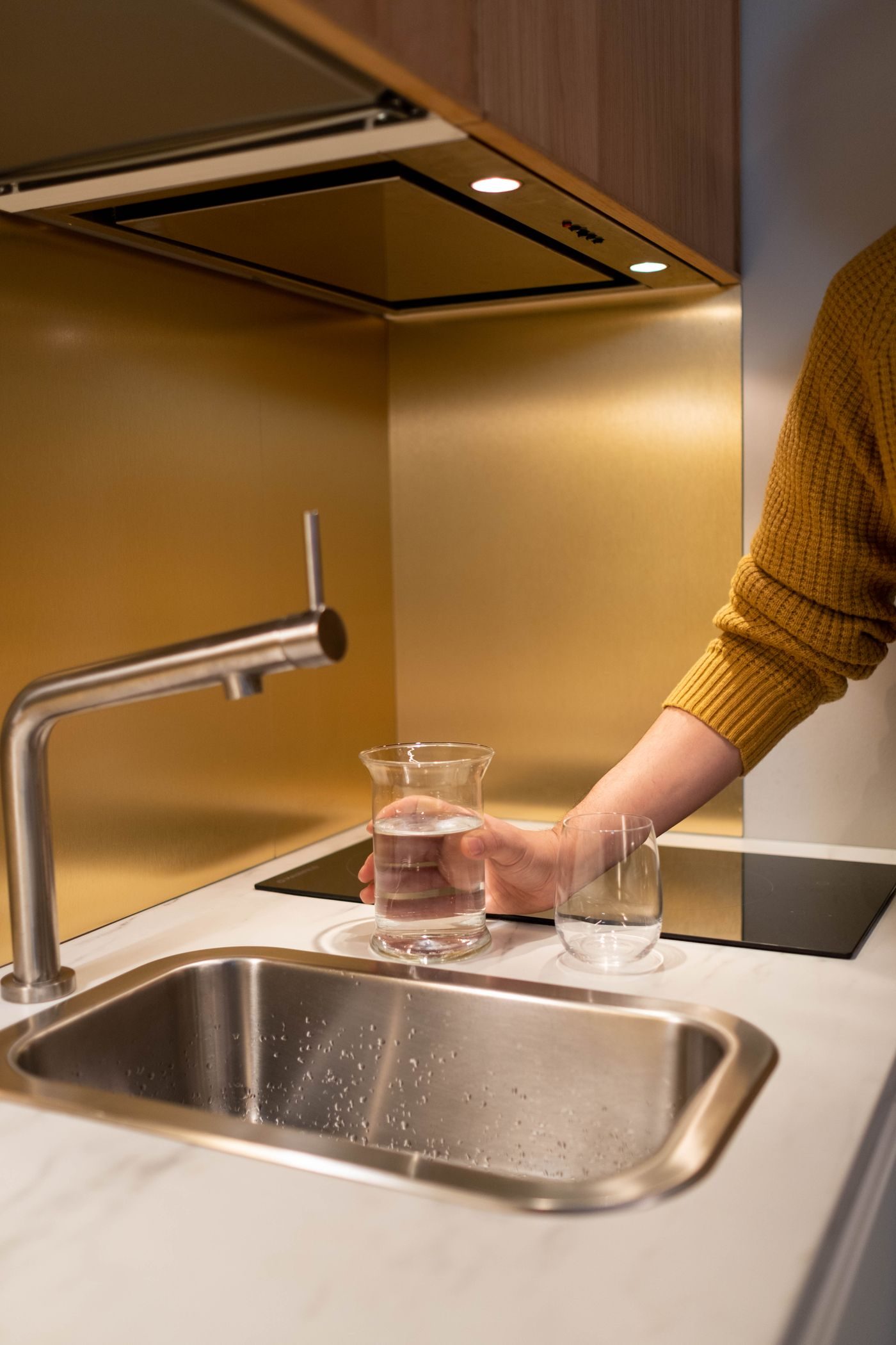 Hand filling a glass from a kitchen tap under warm light